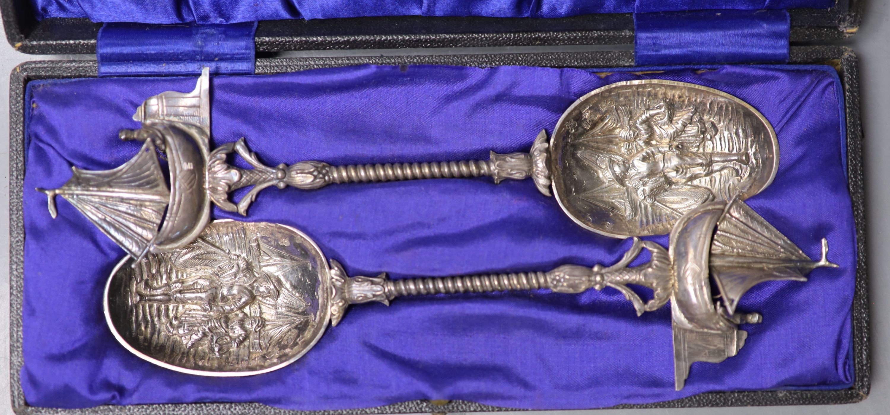 A cased pair of early 20th century Hanau white metal serving spoons, with embossed bowls and yacht terminals, with Dutch import marks, 21.5cm, 165 grams.